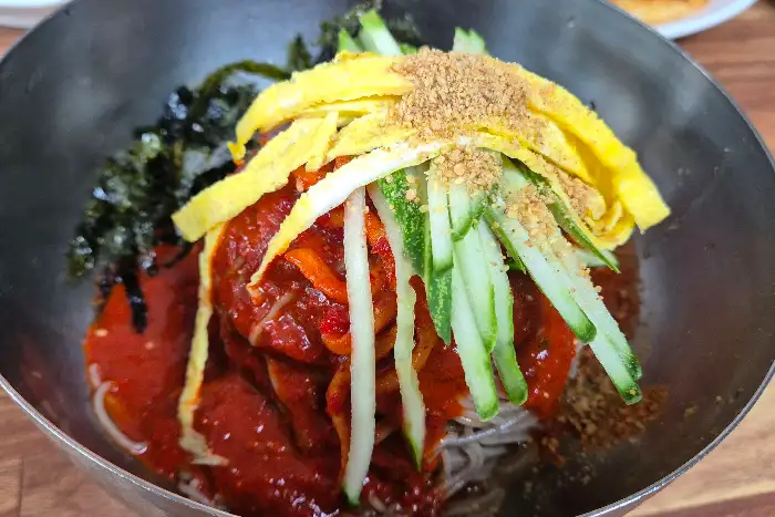 먹음직스러운 비빔 막국수에 고명으로 올라간 계란 지단과 오이