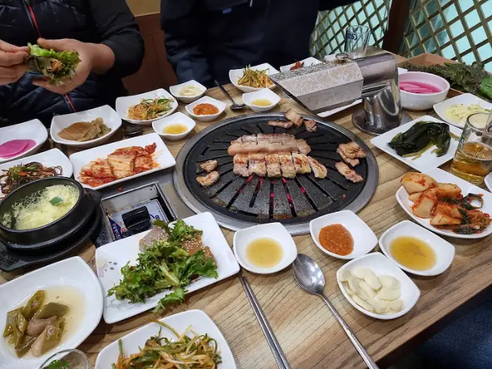 숯불 위에서 구워지고 있는 삼겹살과 함께 차려진 푸짐한 한상차림