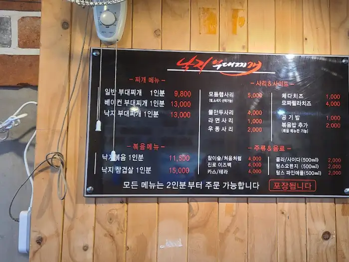 벽면에 부착된 메뉴판으로, 다양한 찌개와 볶음, 사리 메뉴의 가격이 기재되어 있습니다.
