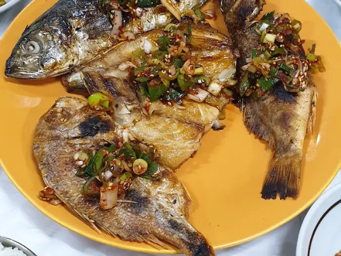 노란 접시에 담긴 명촌식당의 생선구이, 짙은 색감의 양념과 어우러져 더욱 먹음직스럽습니다.