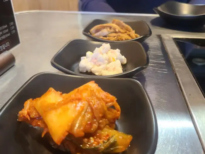 김치, 멸치볶음, 샐러드 등 세 가지 곁들임 반찬이 검은색 접시에 담겨 있습니다.