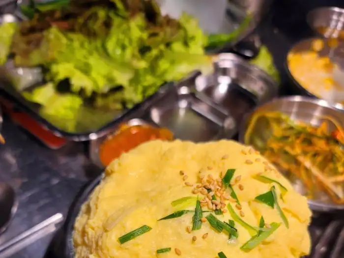 테이블 위에 여러 반찬과 쌈 채소가 놓여 있다.