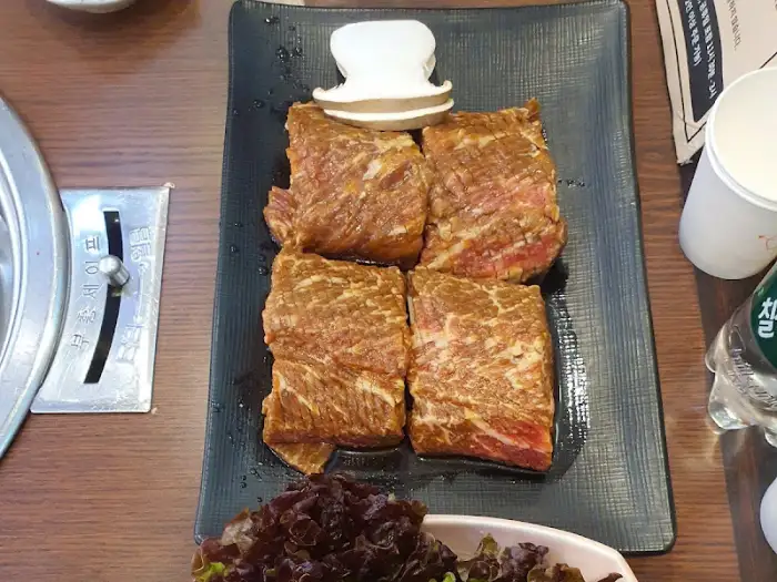 블랙 접시에 담긴 두툼한 갈비 4조각과 버섯