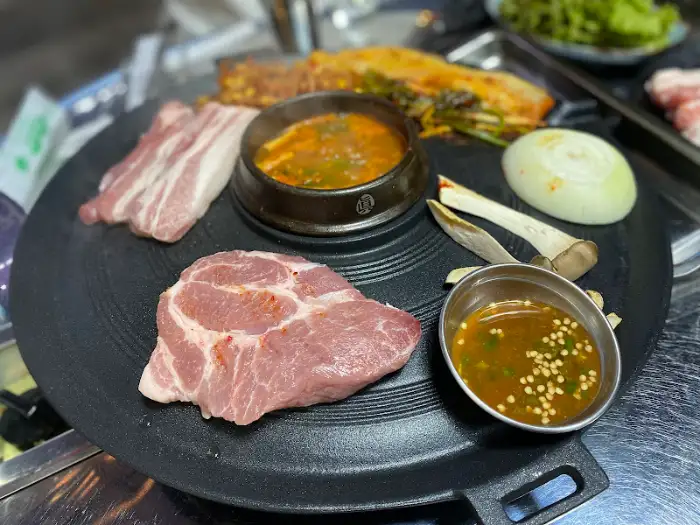 돌판 위에 올라간 삼겹살, 목살, 김치찌개, 소스 등이 세팅된 모습