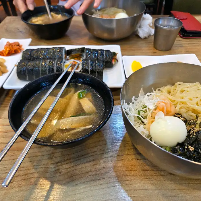 테이블에 놓인 김밥, 맑은 국물, 그리고 비빔국수로 보이는 음식이 정갈하게 준비되어 있습니다.
