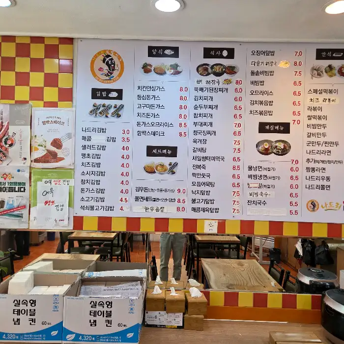 음식점 내부 벽에 걸린 메뉴판과 다양한 음식 사진들이 보입니다.