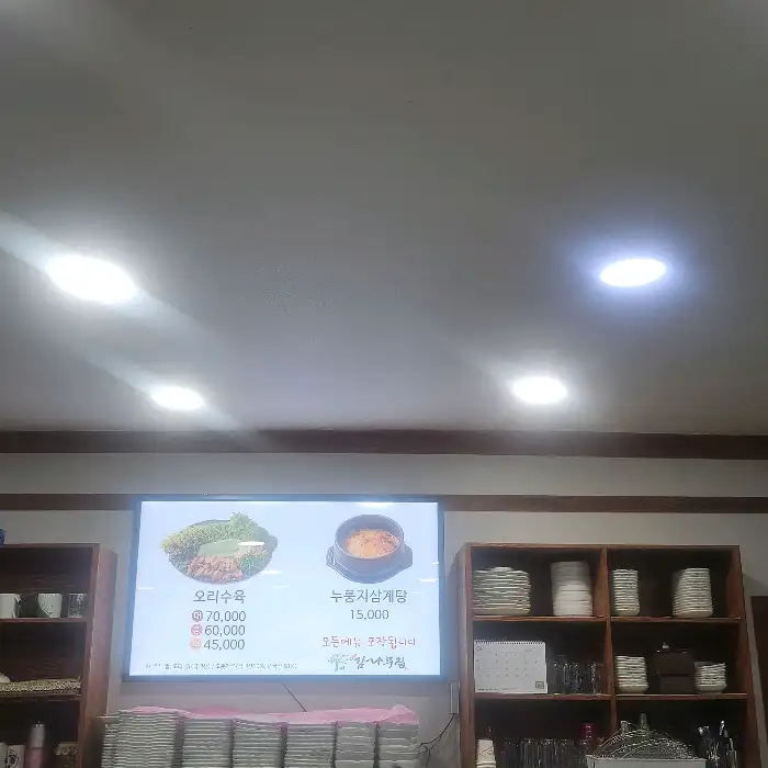 벽에 걸린 TV 화면에 오리수육과 누룽지삼계탕 메뉴가 표시된 모습
