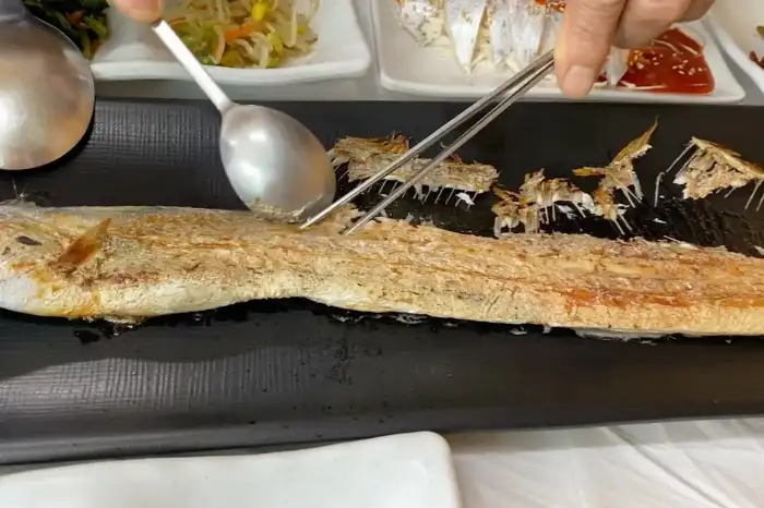 손으로 집게와 숟가락을 이용해 통갈치구이의 살을 발라내는 모습