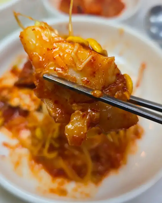 젓가락으로 집어 올린 먹음직스러운 금복이네찜 아구찜 한 점