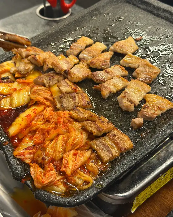 먹기 좋게 잘라진 삼겹살 조각들이 김치와 함께 불판 위에서 익어가고 있는 모습