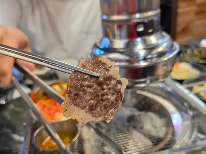 식껍 서대문역 직영점에서 집게로 집어 올린 잘 구워진 고기 한 점
