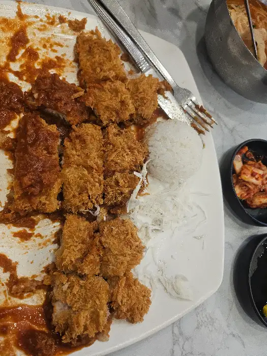 잘라놓은 돈까스가 접시에 가지런히 놓여있고, 밥과 샐러드가 곁들여져 있다. 돈까스는 튀김옷이 바삭해 보인다.