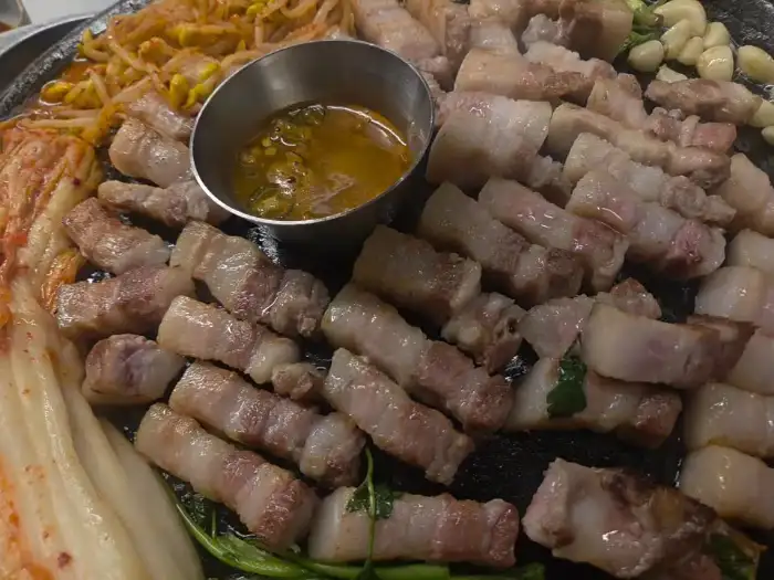 솥뚜껑 위에 김치, 콩나물, 미나리와 함께 올려진 삼겹살